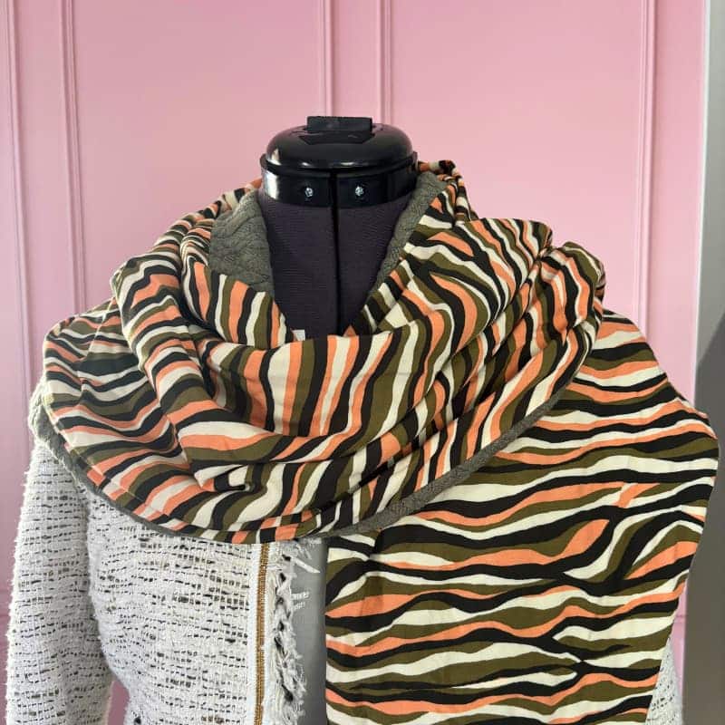 Écharpe triangle femme kaki saumon, tissu imprimé à rayures multicolores, doublure sweat matelassée kaki, mannequin avec veste claire.