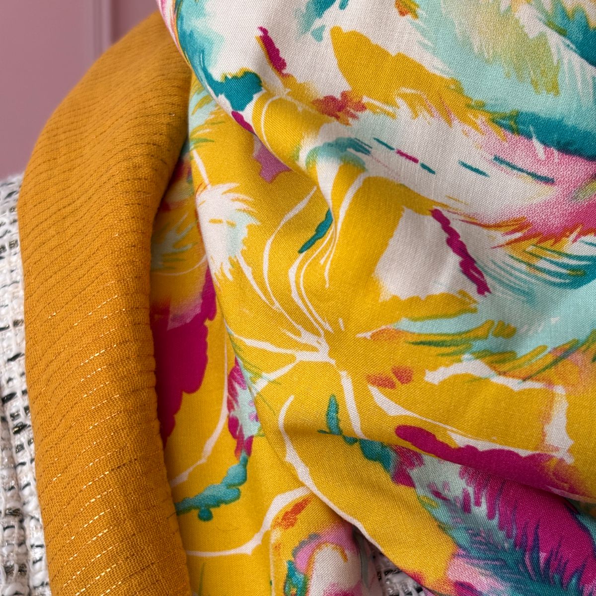 Détail rapproché des tissus du chèche "Pop Folk". On distingue les rayures dorées tissées dans la gaze de coton jaune moutarde et le motif graphique coloré du tissu coton principal.