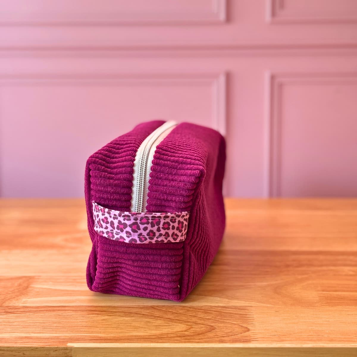 Zoom sur la poignée en coton à motif léopard rose d'une trousse de toilette en velours côtelé violet.