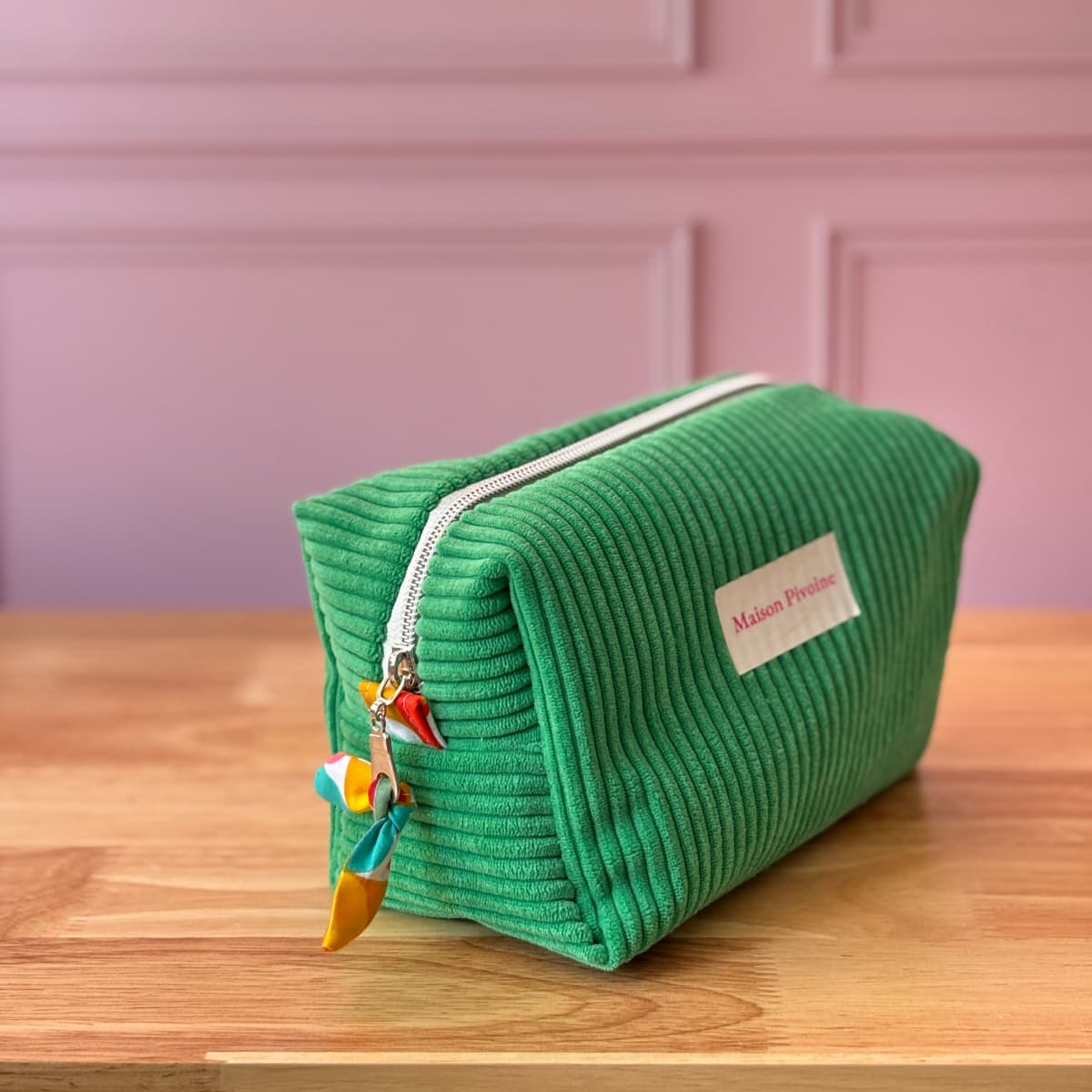 Zoom sur les détails d'une trousse rectangulaire en velours vert, fermeture éclair avec nœud en tissu coloré.