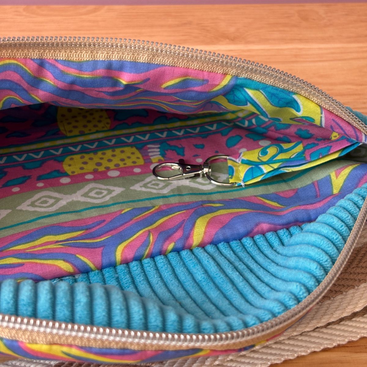 Gros plan de l'intérieur du sac banane turquoise ouvert : doublure coton colorée motifs psychédéliques et cordon à clés.