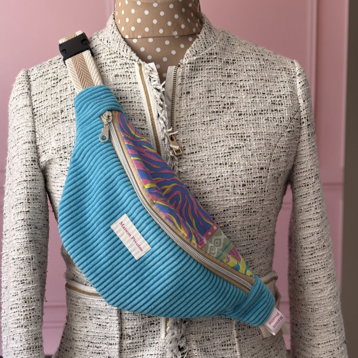 Sac banane en velours côtelé turquoise Maison Pivoine présenté sur un mannequin buste portant une veste texturée beige.