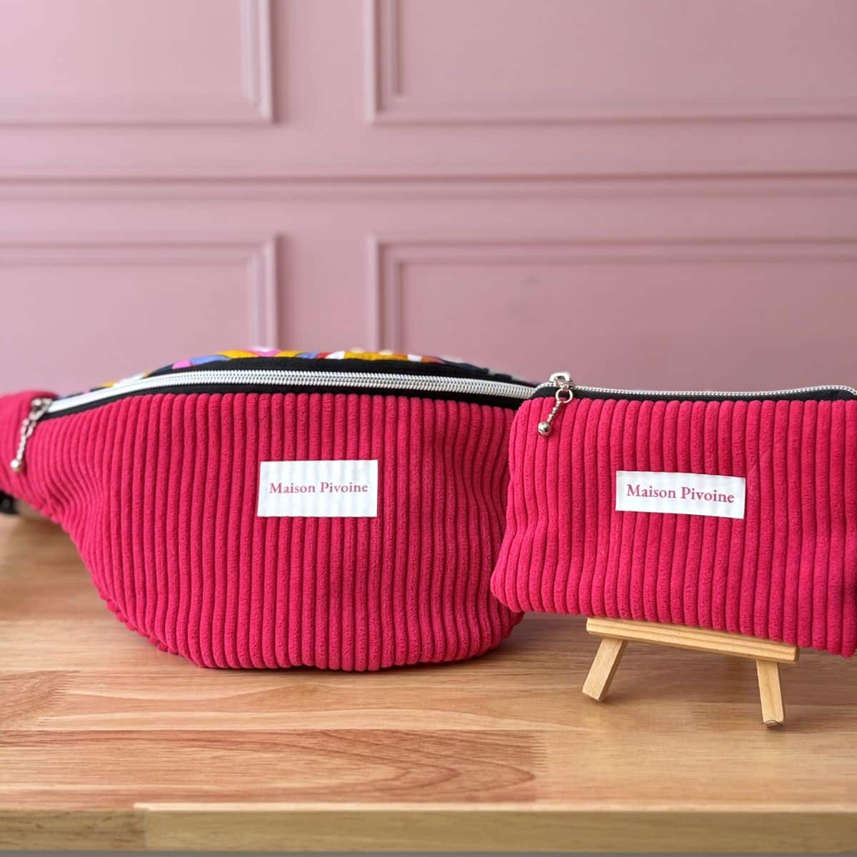 Parure Maison Pivoine fuchsia : sac banane XXL et pochette assortie présentés sur un support en bois.