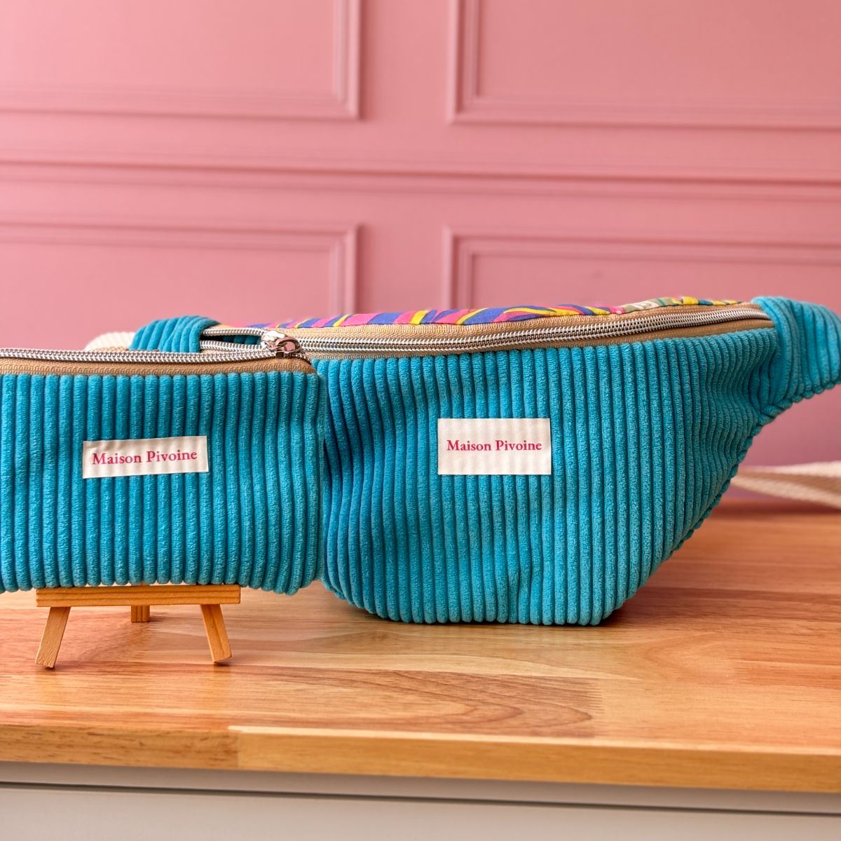 Duo assorti : grand sac banane en velours turquoise et petite trousse assortie posés sur un comptoir en bois.