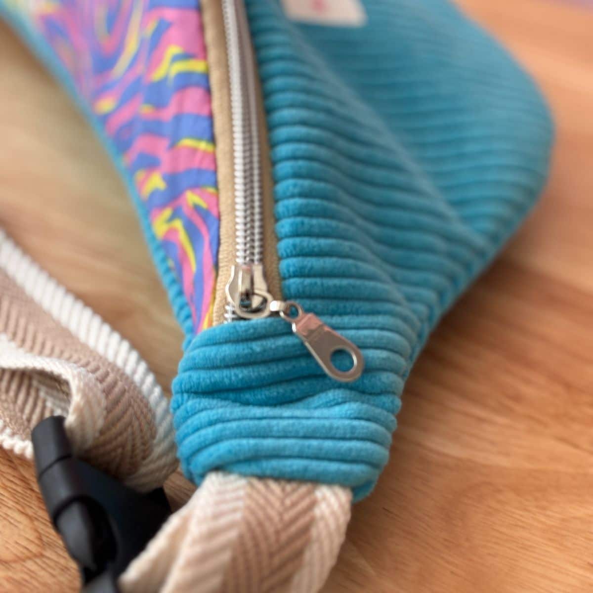 Détail technique du sac banane turquoise : fermeture éclair de qualité et sangle sangle beige réglable avec boucle.