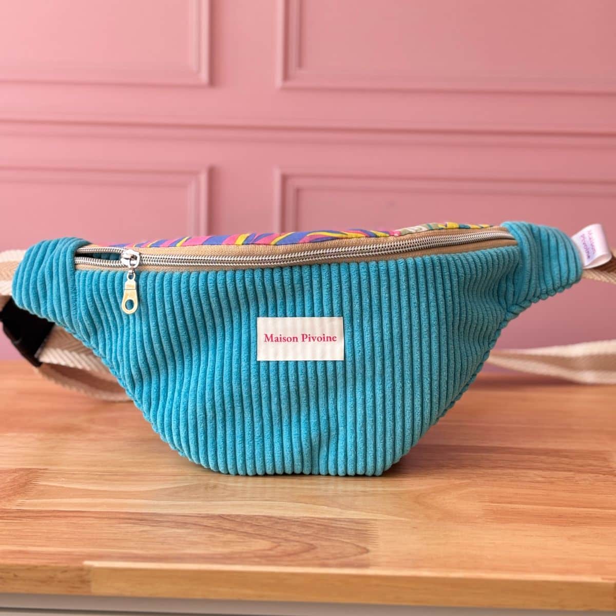 Sac banane en velours côtelé turquoise Maison Pivoine, vue de face avec étiquette de marque blanche, posé à plat