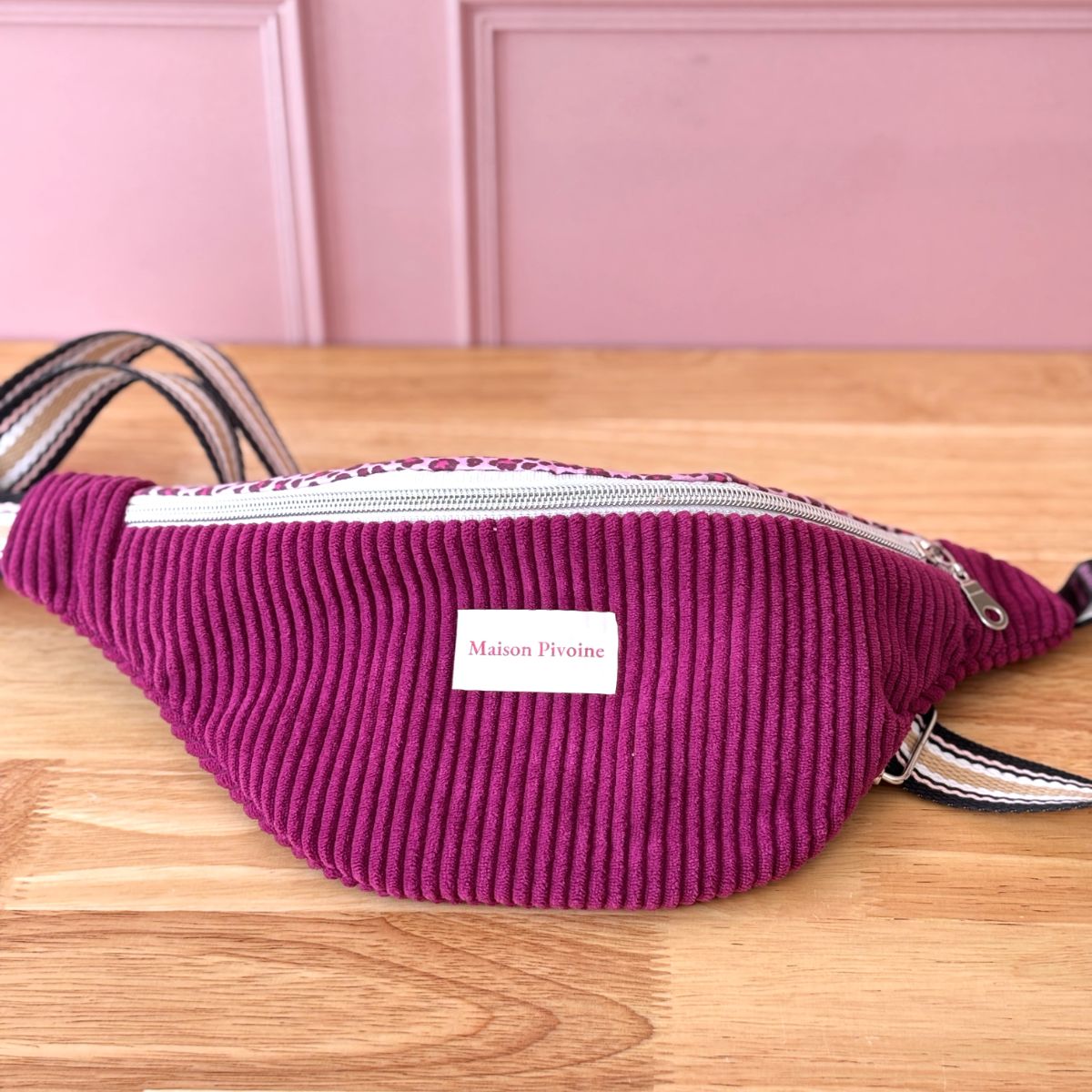 Sac banane prune velours côtelé posé de profil à plat, montrant la sangle motif géométrique noir et blanc