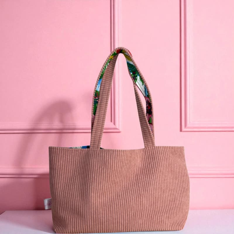 Sac cabas artisanal Maison Pivoine en velours côtelé rose, vu de dos, avec anses doublées d’un tissu fleuri coloré, posé devant un mur rose.