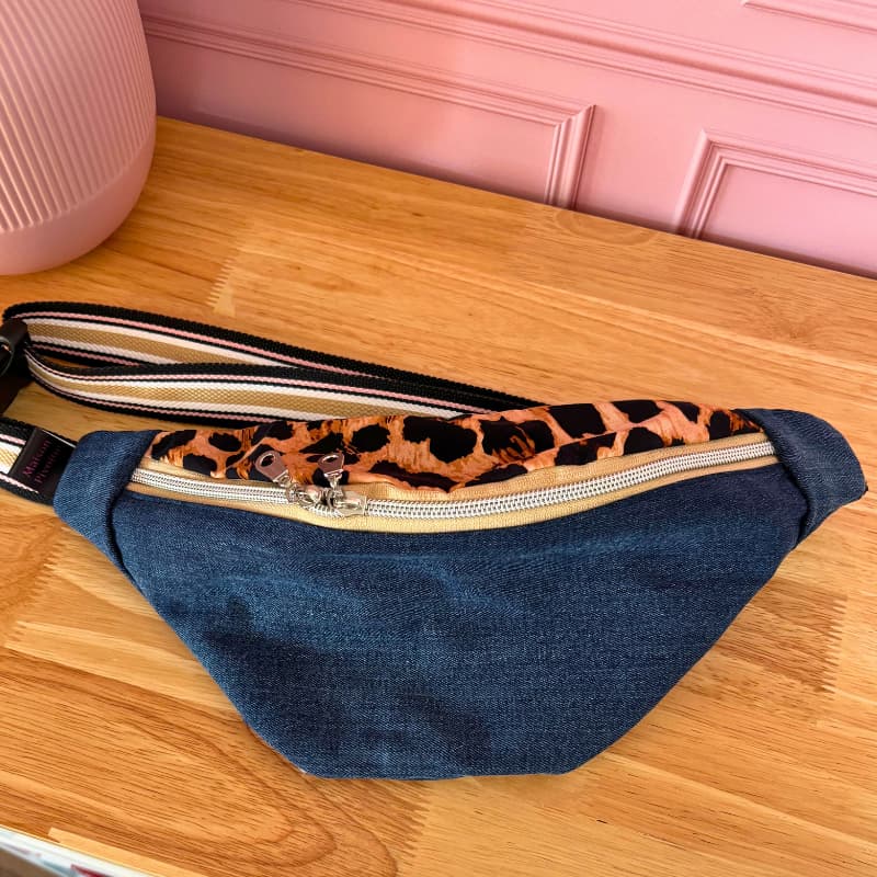 Sac banane Maison Pivoine en jean’s recyclé avec détail de sangle réglable, posé sur une table en bois.