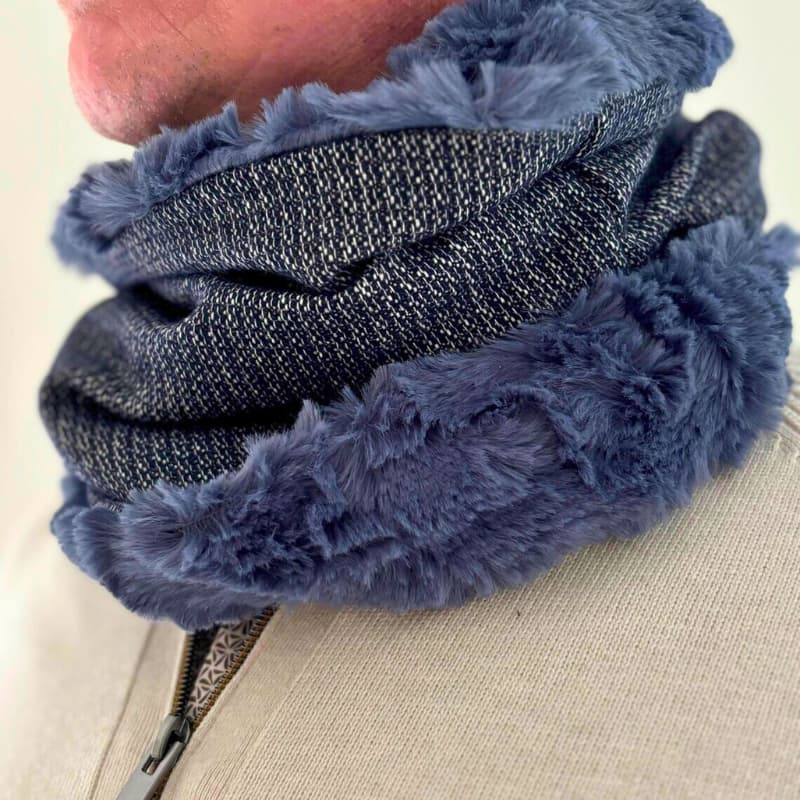 Gros plan d’un homme portant un snood bleu doublé de fausse fourrure, mettant en valeur la texture douce et le tissu extérieur gris chiné.