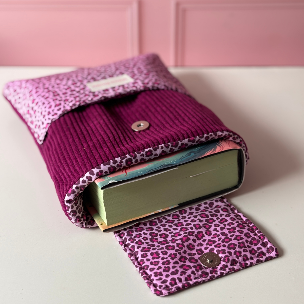 Pochette de protection pour roman en velours côtelé violet prune, avec rabat ouvert et poche avant en tissu imprimé léopard violet et rose.
